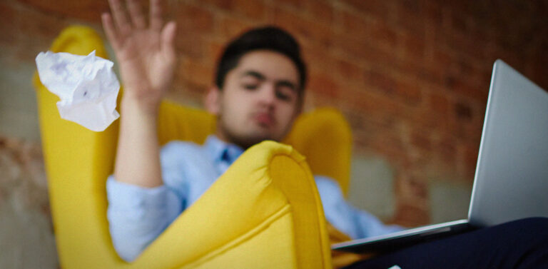 young man sitting in a yellow arm chair on a laptop throwing away a crumpled paper ball