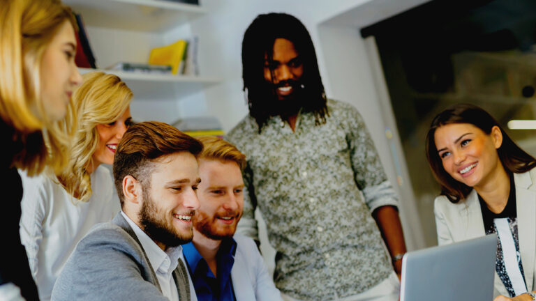 coworkers surround a laptop looking pleased but there is only one Black person