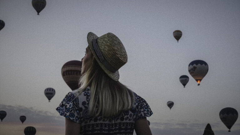 Person starting wistfully at several hot air balloons in a desert sky at dusk